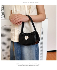 Detailaufnahme einer schwarzen matten Handtasche mit weißem Herz und goldener Schleife