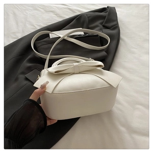 Close-up of stylish beige bow handbag with top handle and matching slim shoulder strap