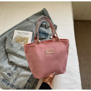 Pink nylon crossbody bag with FASHION patch displayed on bed with a book and jacket