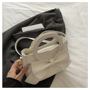 Detailed shot of cream white bow handbag on black blazer with circular ring handle