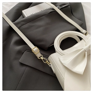 Detail of white leather handbag featuring large bow design and gold metal hook buckles