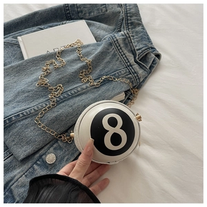Detail of a round billiard number 8 crossbody bag with gold chain strap on denim fabric