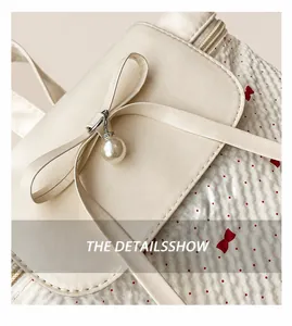 Close-up of cream lace backpack featuring a red bow pattern and pearl pendant detail