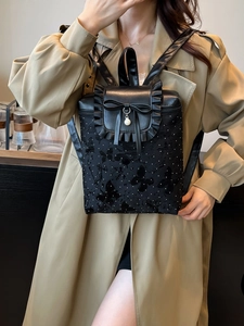 Black ruffled backpack with butterfly prints and pearl bow detail on model in trench coat