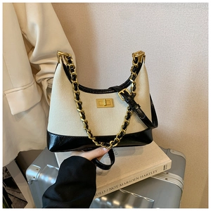 Detail of canvas hobo bag with black leather trim and vintage gold chain on a suitcase