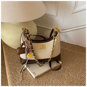 Detail of canvas crossbody bag with leather trim, metal chain, and cute charms on books