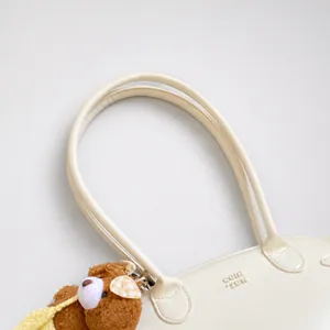 Detail van wit lederen handtas handvat met reliëflogo en bruine pluche beer sleutelhanger