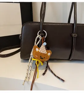 Detail of cute plush bear charm with party hat on brown faux leather tote bag