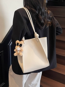Minimalist beige leather tote bag with plush bear charm worn by a model on a staircase