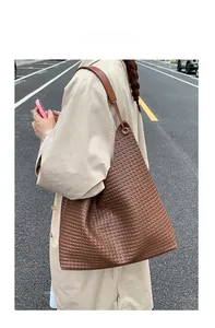 Detail of a brown woven tote bag with leather straps and metal eyelets for women