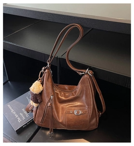 Detail of a brown leather backpack with tassel zipper and a cute teddy bear charm accessory