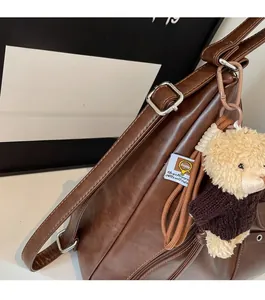 Close-up of brown PU leather backpack with silver hardware and cute teddy bear pendant
