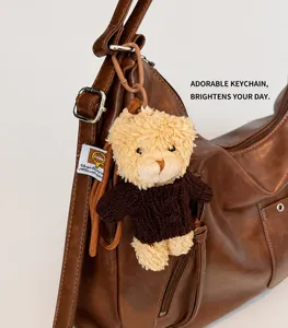 Detail of cute plush bear charm with brown knit sweater hanging on a leather tote bag