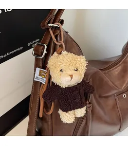 Detail of cute plush bear charm with brown knit sweater hanging on a leather tote bag