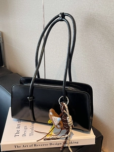 Glossy black faux leather tote bag with plush doll charm and sleek minimalist shoulder straps