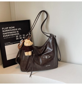 Detail of dark brown faux leather tote with metal buckle and plush bear pendant