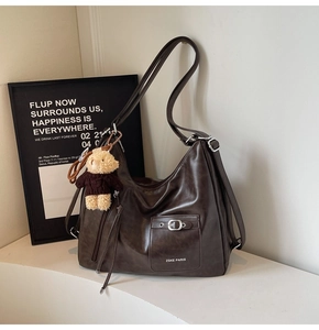 Detail of dark brown tote bag featuring silver buckle pocket and plush bear pendant