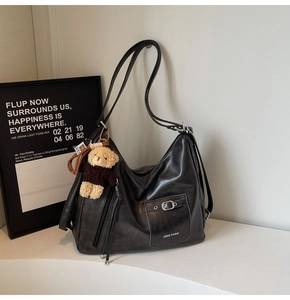 Detail of black leather hobo bag featuring metal buckle pocket and cute teddy bear charm
