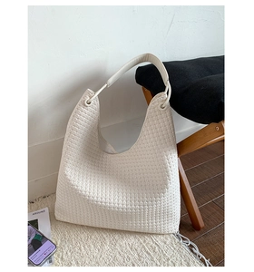Close-up of white woven hobo bag texture with metallic ring details on a soft rug