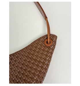 Close-up of brown woven tote bag featuring reinforced eyelets and leather strap texture
