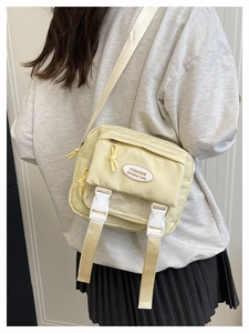Close-up of stylish light yellow crossbody bag with buckle detail and fashion label