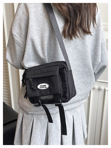 Detailed back view of a black messenger bag styled with a grey hoodie and pleated skirt