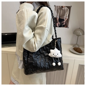 Detail of black quilted tote bag with bear pattern and fluffy cloud charm on shoulder