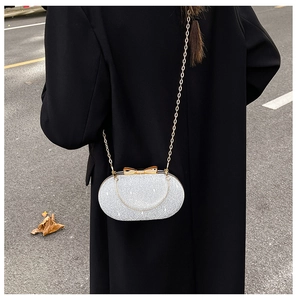 Pochette de soirée argentée avec texture pailletée et fermoir nœud doré sur manteau