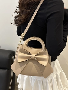 Elegant beige bow handbag with gold hardware and shoulder strap shown in a fashion setting