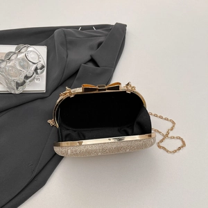 Détail d'une pochette champagne avec fermoir nœud et chaîne dorée sur costume noir