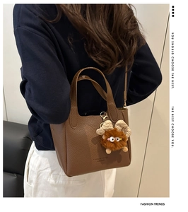 Detail of dark brown pebble leather bucket bag featuring a plush monster charm