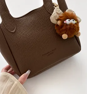 Detailed texture of brown litchi grain leather bucket bag with cute plush monster charm