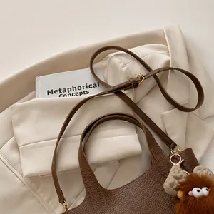 Detail of brown litchi pattern leather bucket bag with cute plush doll pendant accessory