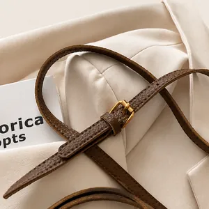 Close-up of brown litchi grain leather strap with gold buckle detail on a bucket bag