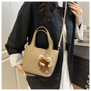 Litchi pattern leather bucket bag with plush charm shown as a crossbody and handbag