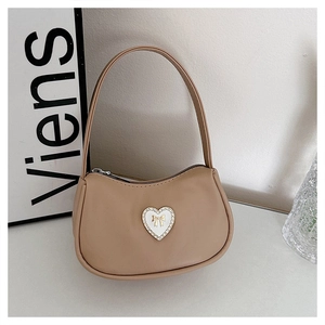 Detail of light brown crescent bag featuring heart-shaped rhinestone and golden bow decor