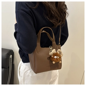 Détail du sac seau en cuir litchi marron avec une breloque monstre en peluche douce