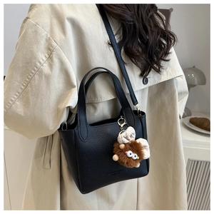 Détail du sac à main noir en cuir grainé avec breloque monstre en peluche sur un trench-coat