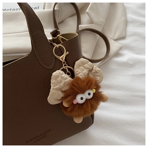 Dettaglio di un ciondolo di peluche marrone con fiocco bianco su una borsa di pelle