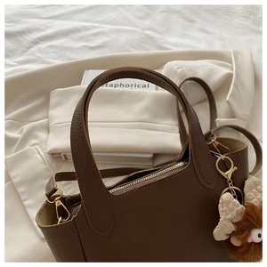 Dettaglio borsa tote marrone in pelle grana con zip dorata e charm mostriciattolo peluche