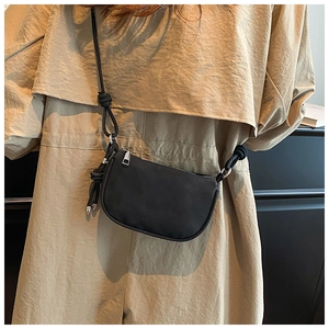 Detail of black minimalist crossbody bag featuring knotted nylon strap and zip closure