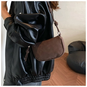 Close-up of brown suede underarm bag with knot detail and embossed logo on shoulder strap