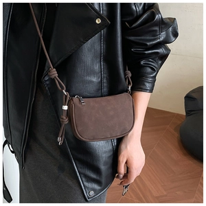 Close-up of brown suede crossbody bag with elegant knot strap and silver zipper detail
