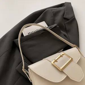 Close-up of cream leather baguette bag with oversized gold metal buckle on gray blazer