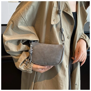 Detail of grey matte saddle bag with knot strap on khaki trench coat, vintage style