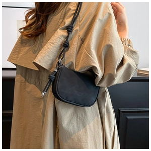 Detail of minimalist black crossbody bag with decorative knotted shoulder strap on trench coat