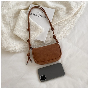 Detail of a brown suede crescent bag with knot strap next to a phone for size comparison