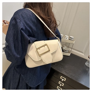 Detail shot of a minimalist cream shoulder bag featuring a large gold rectangular metal buckle