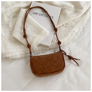 Detail of brown saddle bag with knotted strap and silver metallic tips on tweed fabric
