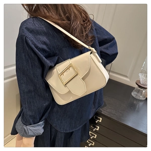 Détail d'un sac à bandoulière crème élégant avec boucle dorée porté par un mannequin